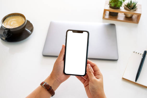 istock hands holding mobile phone with blank screen and laptop computer on the table in office 1184802839