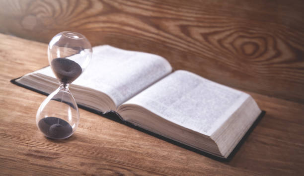 istock Hourglass with book on wooden table. 1184807035