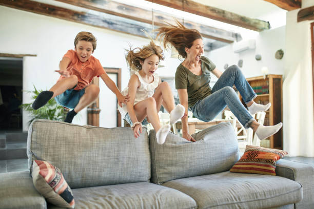 スペインの母と子供がソファの背中を飛び越える - domestic life jumping child sofa ストックフォトと画像