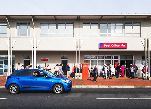 Cape Town, South Africa - November 1, 2019: Social and old-age pensioners queue outside a branch of the South African Post Office early in the morning of the 1st of the month for payment of their state grants. The Post Office acts as an agent of the South African Social Security Agency, which administers the state welfare system, the most comprehensive in Africa.