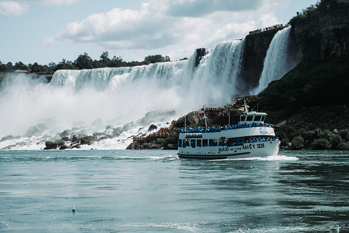 This is a photo of the US side of Niagara Falls with a boat full of people dressed in blue waterproof coats in the foreground.