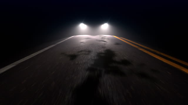 Car with headlights on follows camera tracking along country night road