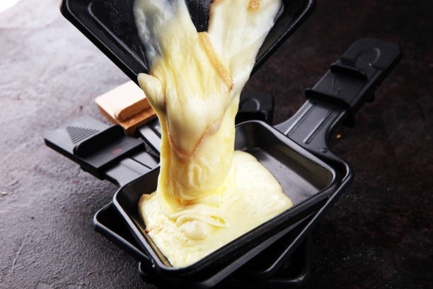 raclette сыр расплавленного подается в отдельных raclette сковородки - raclette cheese стоковые фото и изображения