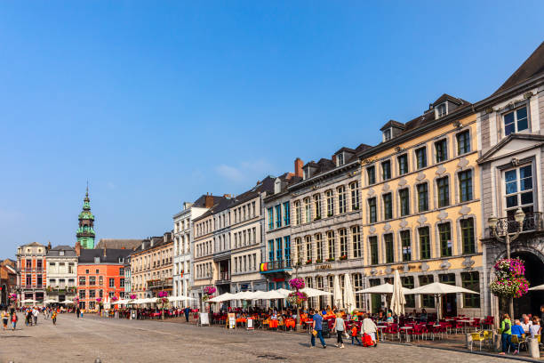 Tourists sitting at the outdoor tables or strolling in the Grand Place, the main square of Mons, one of the beautiful cities in Wallonia.