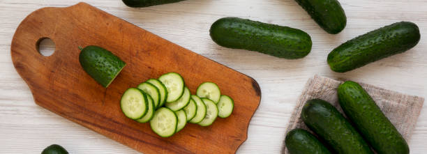 istock Fresh organic mini baby cucumbers on a rustic board on a white wooden surface, top view. Flat lay, from above, overhead. 1184827687