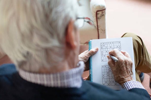 uomo anziano che fa sudoku puzzle a casa - brain case foto e immagini stock