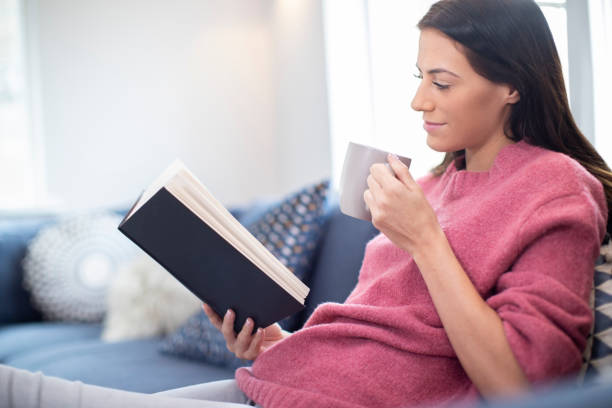 istock Woman With Hot Drink Relaxing On Sofa At Home Reading Book 1184829053