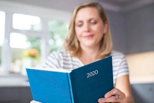 Woman Opening New Year 2020 Diary On Table At Home