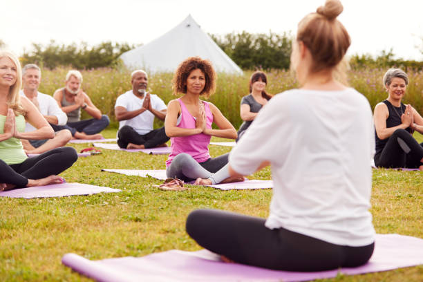 Female Teacher Leading Group Of Mature Men And Women In Class At Outdoor Yoga Retreat Female Teacher Leading Group Of Mature Men And Women In Class At Outdoor Yoga Retreat yurt photos stock pictures, royalty-free photos & images