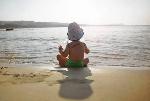 Small child  kid boy sitting on the beach  in beautiful summer day looking far away.  Happy lifestyle childhood concept. View from back.  Cyprus , Ayia-napa