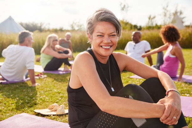 verticale de femme mûre sur la retraite extérieure de yoga avec des amis et le camping à l'arrière-plan - yoga men women exercising photos et images de collection