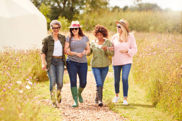 groep volwassen vrouwelijke vrienden wandelen langs pad door yurt camping - mature woman stockfoto's en -beelden