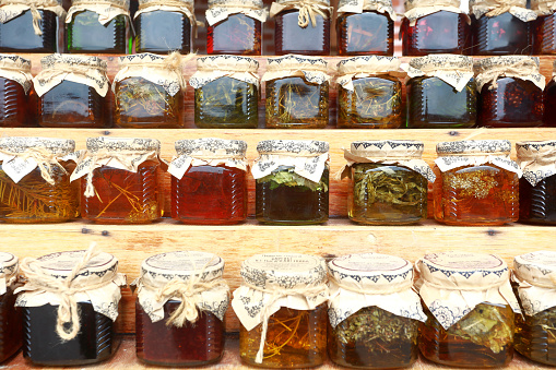 Glass jars with jam and honey standing on shelves at a market. Traditional Harvest Fair