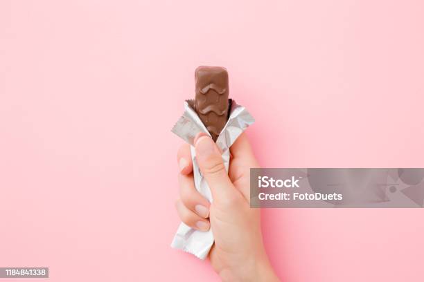 Young Woman Hand Holding Chocolate Bar On Pastel Pink Table Opened Pack Sweet Snack Closeup Top View Stock Photo - Download Image Now