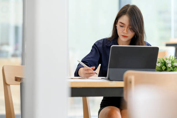 istock Young woman holding pen and working with laptop while sitting in  co-workspace. 1184841960