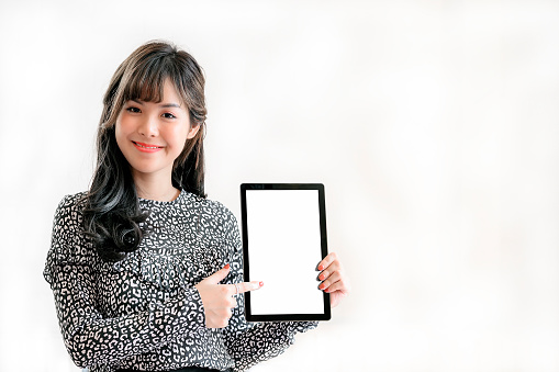 Portrait of beautiful asian woman looking at camera, smiling and holding digital tablet with white screen. Copy space and isolated on white background.