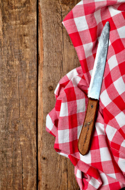 istock Knife on red checkered tablecloth right frame on vintage wooden table background - view from above - vertical photo 1184846244