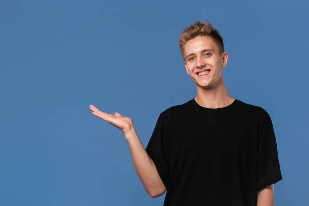 istock Handsome young man in a black tee pointing  at the empty space for advertising at a palm of his hand. Copy space 1184847432