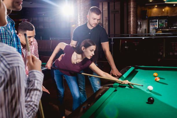 istock Group of young cheerful friends playing billiards. 1184853400
