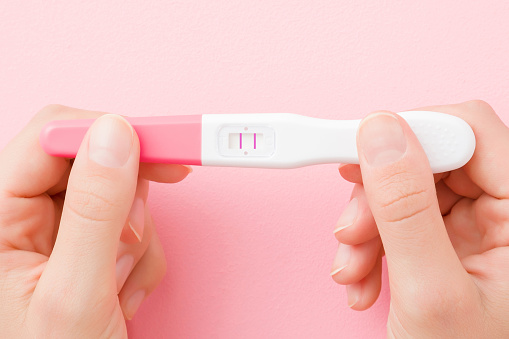 Manos de mujer joven sosteniendo la prueba de embarazo con dos rayas sobre fondo rosa pastel. Resultado positivo. Closeup. Disparo de punto de vista. Vista de arriba hacia abajo. photo