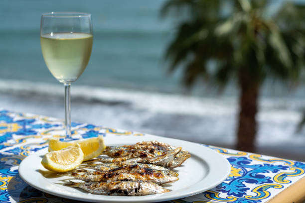Espeto, Malaga style fish on stick barbecue prepared on olive tree firewoods and white wine Sardines espeto, Malaga style fish on stick barbecue prepared on olive tree firewoods on beach served with white wine sardine photos stock pictures, royalty-free photos & images