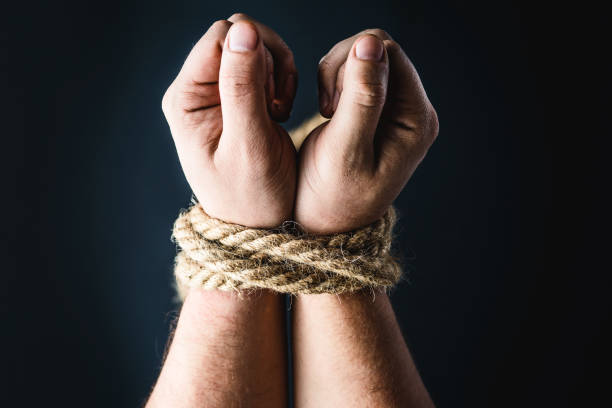 istock hands tied with rope on black background 1184865879