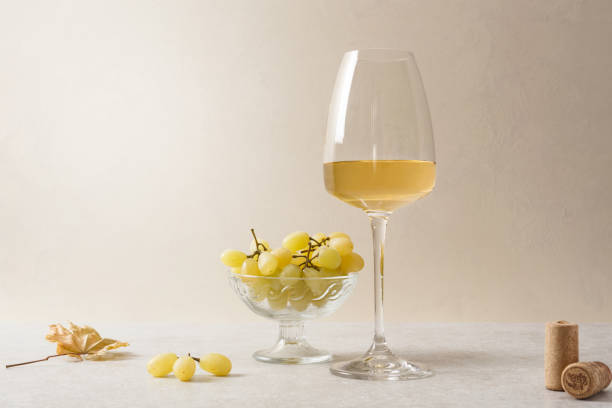 A glass of white wine, grapes and corks on the table. Light background.