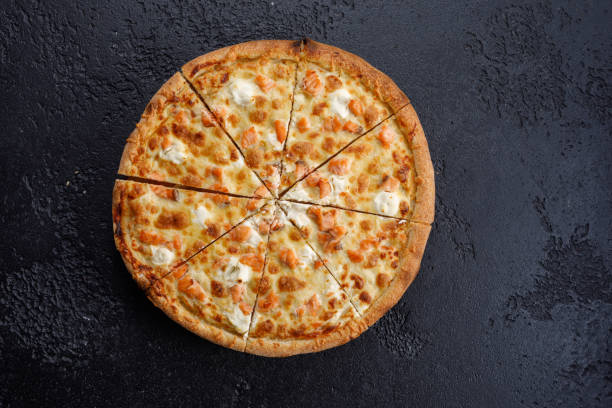 istock Pizza sliced with salmon and cheese on a black textural background. Close-up. The concept of delicious food. View from above. 1184875105