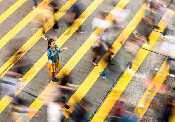 A woman has a moment of peace and calm on a crowded crosswalk in Hong Kong. The crowds crossing the street are blurred by a long exposure.