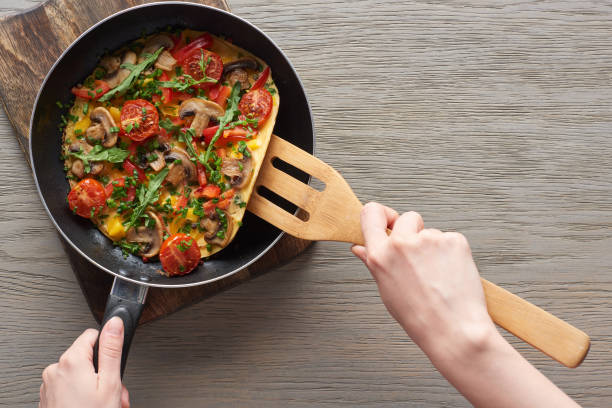 vue recadrée de l'omelette de cuisson de femme avec des champignons, des tomates et des verts sur la poêle avec la pelle en bois - spatula photos et images de collection