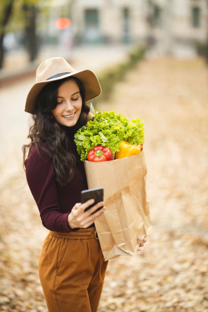 istock Woman using phone and holding grocery bag 1184877770
