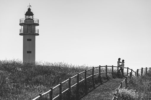 Couple in love outdoors, near a lighthouse, on a wooden fence.  Monochrome version.
