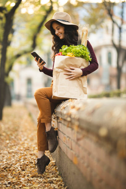 istock Woman using phone and carrying grocery bag 1184884298