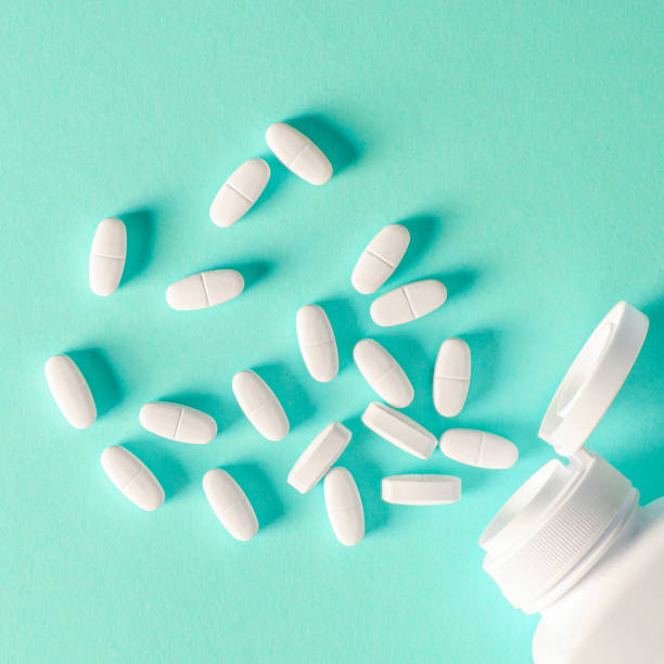 istock A white plastic container with white tablets lies on a multi-colored background next to white tablets 1184886470