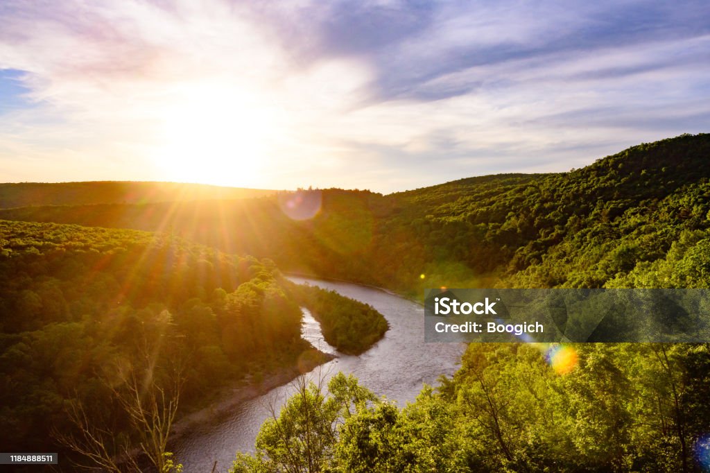Scenic Delaware River Landscape in the Catskill Mountains and New York State Line This is a photograph of the Delaware River winding through the Catskill Mountains and creating a natural state line between New York and Pennsylvania. The setting sun shines across the water and treetops in summer. Pennsylvania Stock Photo