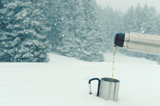 Drink hot tea from thermos during winter walk in the snowy forest, Italy