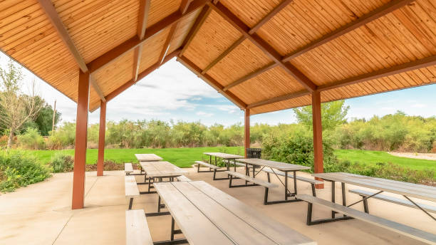 istock Panorama frame Row of white tables with seats under a pavilion with brown ceiling at a park 1184893498