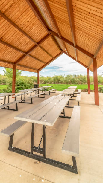 istock Vertical Row of white tables with seats under a pavilion with brown ceiling at a park 1184896046