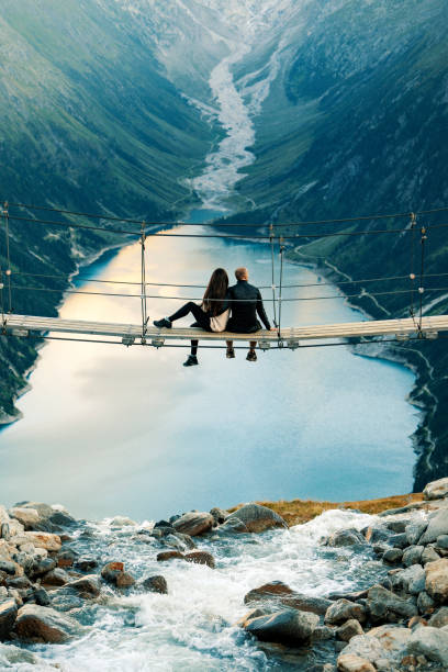 Love at high altitudes Happy couple on holiday. Mountain landscape. Boyfriend sitting with his girlfriend on rope brige. Romantic moment after proposal or engagement. Passionate lovers on summer vacation. Couple in love enjoying the view from Schlegeis Stausee (Schlegeis Lake) in Tyrol, Austria. Man and his girlfriend at Schlegeis glacier and beautiful blue lake in the mountains of Tirol, Austria. tyrol state austria stock pictures, royalty-free photos & images