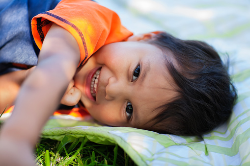 The cute smile of a young boy that is laying down on a picnic blanket, that awoke from a daytime nap.