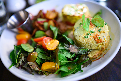 This is a photograph of a vegan “eggs Benedict” made from tofu served on a plate with a fresh green salad in Brooklyn, New York.