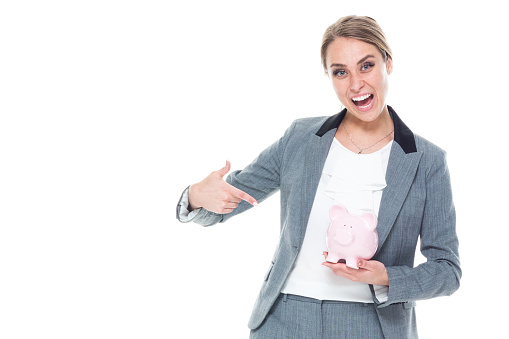 One person / front view / waist up of 20-29 years old adult beautiful caucasian female / young women businesswoman / business person standing in front of white background wearing a suit who is smiling / happy / cheerful / successful and holding piggy bank / currency / investment / retirement / savings / wealth