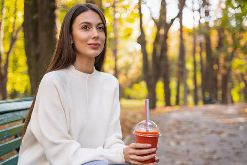 Good-looking young woman sitting on a bench with a drink in her hands