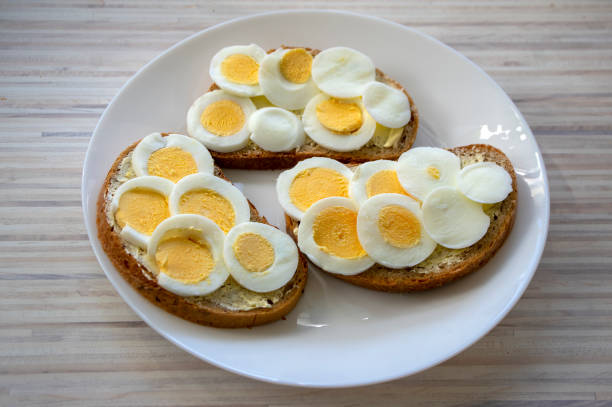 Sliced hard boiled eggs on common czech bread on white plate on light wooden table, simplicity delicious breakfast