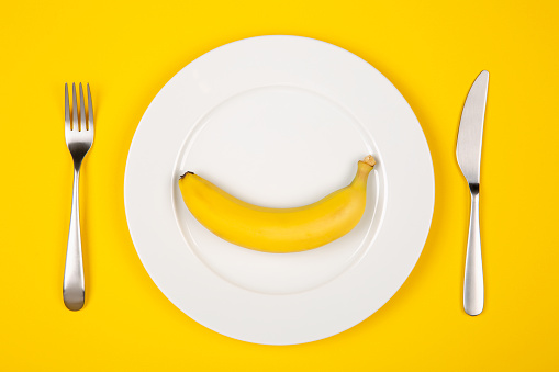 Banana served on the white dish isolated on yellow. Vegetarian or vegan diet