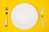 A plate, knife and fork set isolated on yellow background