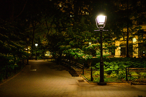 This is a color photograph of the sidewalk illuminated with street lamps on a spring night in Washington Square Park in New York City.