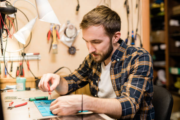 istock Repairman bending over broken gadget and using screwdriver to fix tiny parts 1184924257