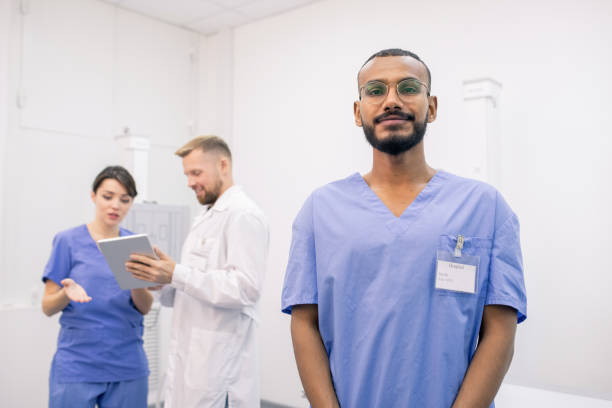 istock Young bearded mixed-race intern standing on background of two colleagues 1184925773