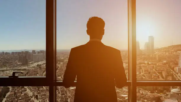 Photo of Successful businessman is looking at panoramic city view from his modern apartment.